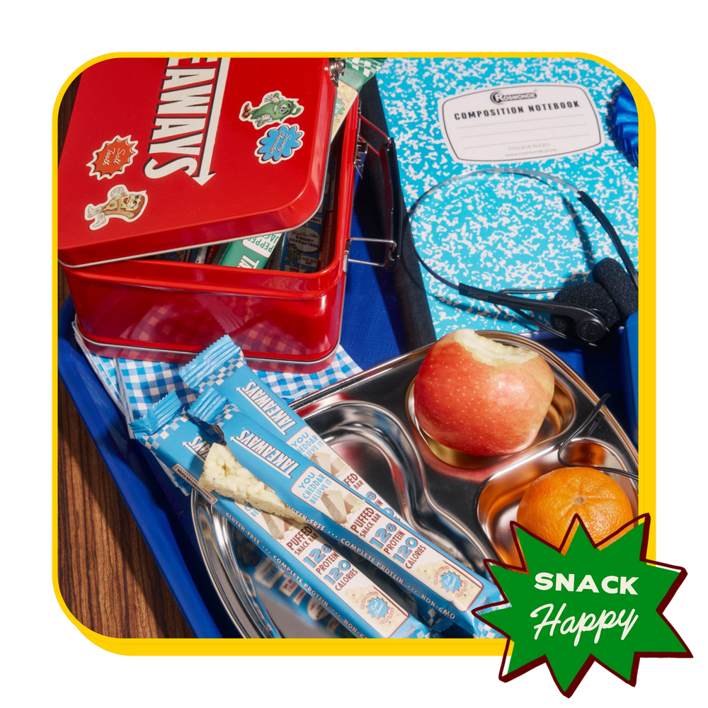 Takeaways White Cheddar protein bars in a retro lunchbox tray with an apple, orange and composition notebook
